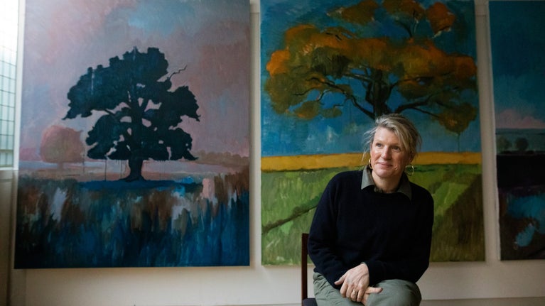 Woman sat smiling on a stool in a studio with large paintings behind